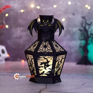 May include: A black Halloween lantern with a bat on top and cut-out designs of spiders, witches, and haunted houses. The lantern is illuminated from within, creating a spooky glow. The lantern is made of paper.