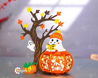 May include: A decorative Halloween-themed papercraft featuring a tree with fall leaves, a ghost, and a pumpkin lantern. The pumpkin lantern has a ghost wearing a hat that says "FALL" and is reading a book. A small pumpkin is also present.