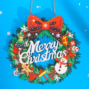 Könnte beinhalten: Ein dekorativer Weihnachtskranz mit einer großen roten Schleife oben, grünem Laub und dem weißen Schriftzug Merry Christmas. Der Kranz ist mit einem Lebkuchenmann, einem Schneemann, Geschenken, Zuckerstangen und weißen Schneeflocken verziert.