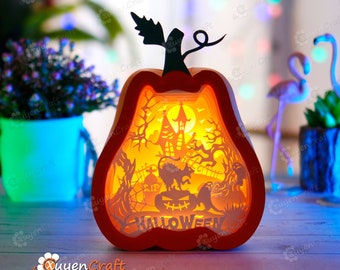 May include: A layered, illuminated pumpkin-shaped Halloween decoration. The orange frame surrounds a detailed scene with a haunted house, trees, a black cat, and the word "HALLOWEEN". The pumpkin has a black stem and leaf.