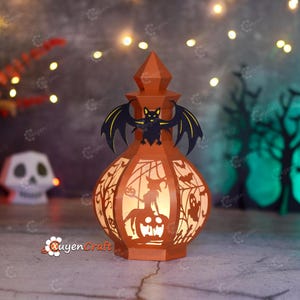 May include: An orange Halloween lantern with a bat on top and cut-out designs of a witch, ghosts, and trees. The lantern is lit from within, creating a warm glow. The lantern is made of paper and has a unique, festive design.