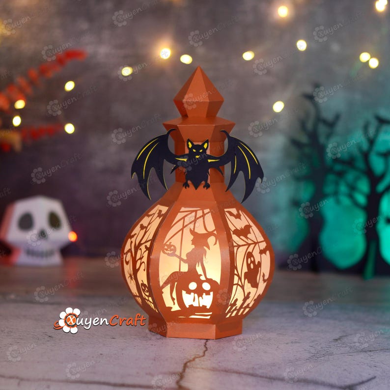 May include: An orange Halloween lantern with a bat on top and cut-out designs of a witch, ghosts, and trees. The lantern is lit from within, creating a warm glow. The lantern is made of paper and has a unique, festive design.
