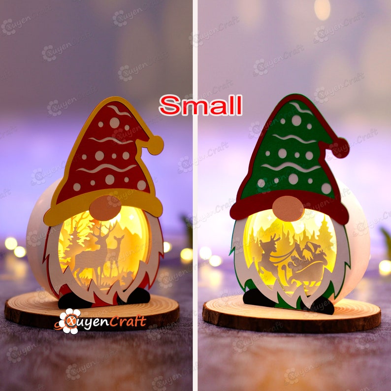 Pode incluir: Duas pequenas lanternas de gnomo de Natal, uma com chap&eacute;u vermelho e outra com chap&eacute;u verde. Cada lanterna tem um design recortado de uma cena de inverno com veados e o tren&oacute; do Papai Noel, e assenta sobre uma base de madeira. A palavra "Small" est&aacute; em texto vermelho.