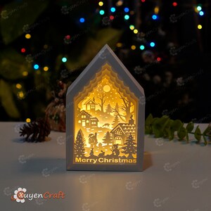 May include: White wooden house shaped light-up Christmas decoration with a cut-out winter scene and the words "Merry Christmas" on the front.