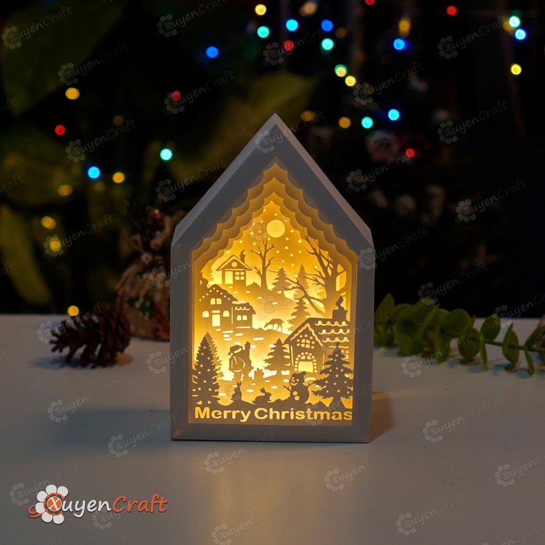 May include: White wooden house shaped light-up Christmas decoration with a cut-out winter scene and the words "Merry Christmas" on the front.