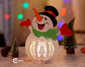 May include: A white snowman papercraft with a red hat, green scarf, and orange nose. The snowman is holding up its arms with red mittens. The snowman is illuminated from within, creating a warm glow.