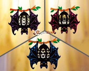 May include: Three hanging bat decorations with black wings and colorful accents. The bats have a black body with a white face and eyes. The wings are decorated with purple, pink, and blue polka dots. The bats are hanging from a branch with green leaves.