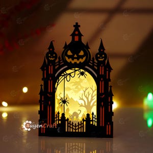 Peut inclure: Une décoration d'Halloween en papier noir découpé au laser représentant la silhouette d'un château hanté avec une arche centrale. Le motif inclut une citrouille, une araignée, une toile, une sorcière, un arbre dénudé et un chat, éclairés.