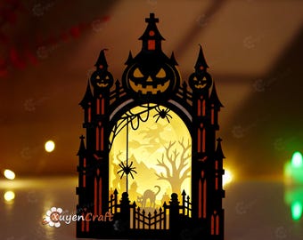 May include: A black laser-cut paper Halloween decoration featuring a haunted castle silhouette with a central archway. The design includes a jack-o'-lantern, a spider, a web, a witch on a broomstick, a bare tree, and a cat, all illuminated from behind.