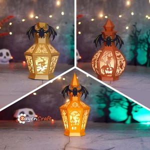 Könnte beinhalten: Drei Halloween-Papierlaternen in Gold-, Orange- und Rosttönen. Jede Laterne hat aufwendige Ausschnitte von Fledermäusen, Hexen und gruseligen Szenen. Die Laternen sind mit einer Fledermaus-Silhouette gekrönt.
