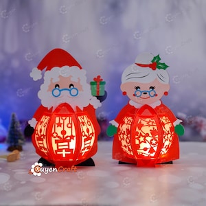 May include: Red and white papercraft Christmas lantern with a Santa Claus design. The lantern is illuminated from within, creating a warm glow. The lantern features a Santa Claus holding a gift and a woman with a white beard and a red hat.