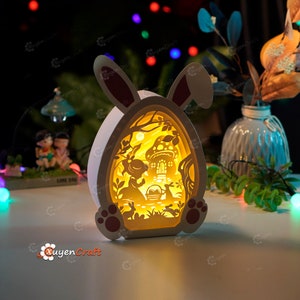 May include: A white wooden Easter bunny night light with a cut-out design of a girl and a bunny rabbit in a forest setting. The light is illuminated from the inside, creating a warm glow.
