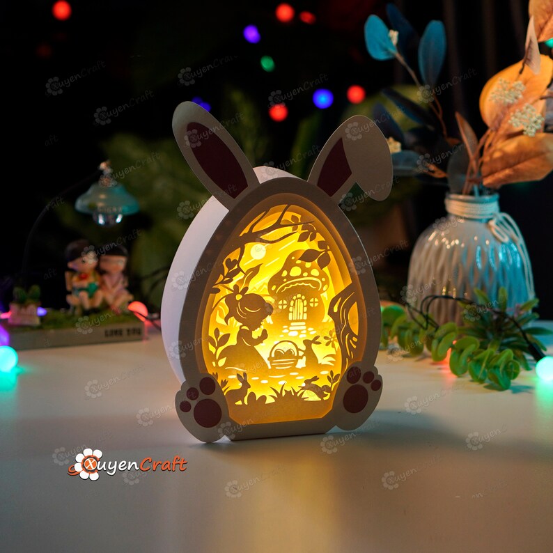 May include: A white wooden Easter bunny night light with a cut-out design of a girl and a bunny rabbit in a forest setting. The light is illuminated from the inside, creating a warm glow.