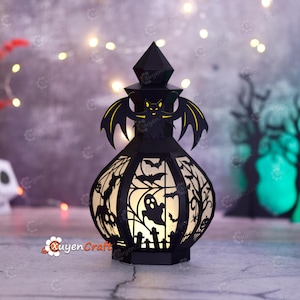 May include: Black Halloween lantern with a bat and spooky silhouettes. The lantern features a geometric design with cut-out bats, ghosts, and trees. The lantern is lit from within, creating a warm glow. The lantern is a decorative item for Halloween.