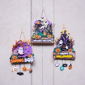 Puede incluir: Tres letreros de pared de Halloween de madera en capas con colgadores de cuerda. Un letrero muestra un fantasma en un columpio con el texto SWING BOO, otro una bruja en una escoba con WITCHES WELCOME y otro una casa embrujada con el texto HAPPY HALLOWEEN.