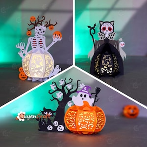 以下が含まれることがあります： ハロウィーンをテーマにした3つの紙製ランタン。1つはカボチャを持った骸骨、もう1つは猫のような姿、3つ目はカボチャのランタンを持った幽霊です。すべて白、オレンジ、黒です。