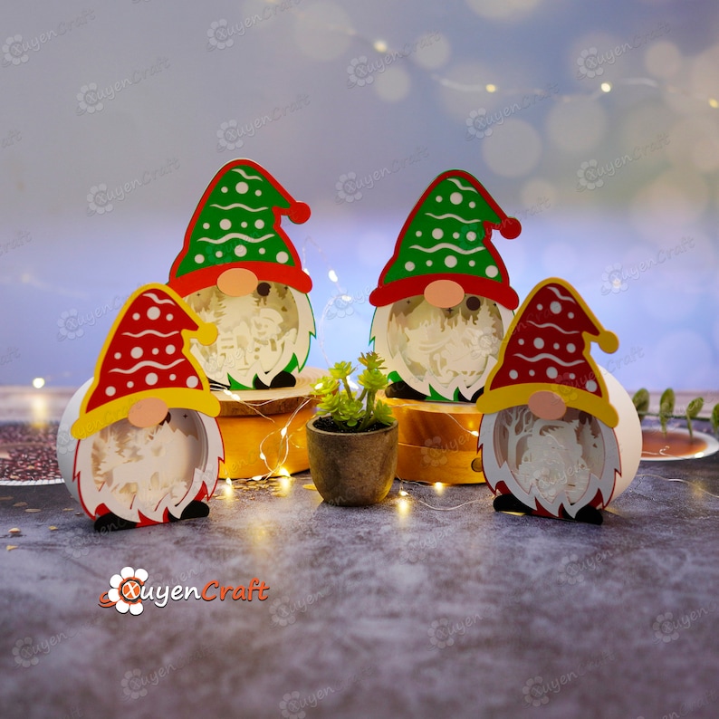 Pode incluir: Quatro decora&ccedil;&otilde;es de Natal de gnomos com chap&eacute;us vermelhos, verdes e amarelos. Cada gnomo tem uma barba branca e um corpo redondo com uma cena interior detalhada. Uma pequena planta em vaso est&aacute; colocada entre dois dos gnomos.