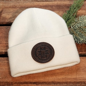 May include: White knit beanie with a brown leather patch featuring a star design and the text "The North Star" in a circle.