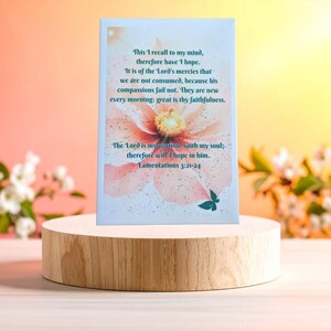 May include: A rectangular card featuring a soft pink flower background with dark teal text that reads: This I recall to my mind, therefore have I hope. It is of the Lord's mercies that we are not consumed, because his compassions fail not.