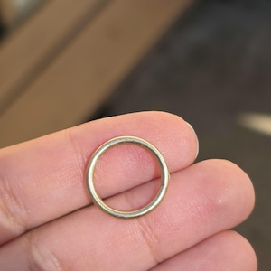 May include: A simple, circular gold-toned metal ring with a smooth, polished surface. The band has a consistent, thin width throughout its entire circumference, presenting a clean and unadorned design that forms a perfect, continuous circle.