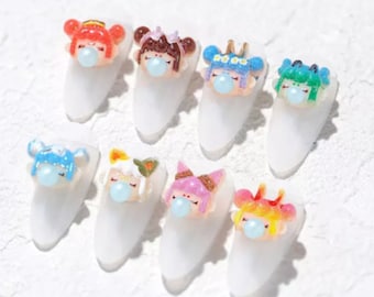 May include: Eight colourful cartoon character nail charms with bubblegum. Each charm is attached to a clear nail tip.