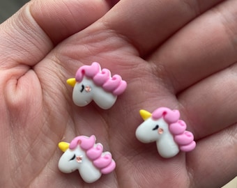 May include: Three small white unicorn figurines with pink manes and yellow horns. The unicorns have pink cheeks and sparkly eyes.