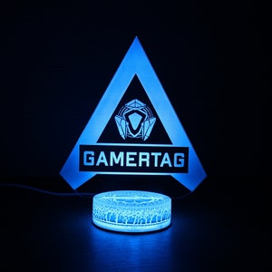 May include: A blue and white gamertag light with a triangle shape and the word "GAMERTAG" printed on it. The light is on a round base.