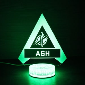 May include: A green triangle-shaped LED night light with a white logo and the word "ASH" in the center. The light is on a white circular base.
