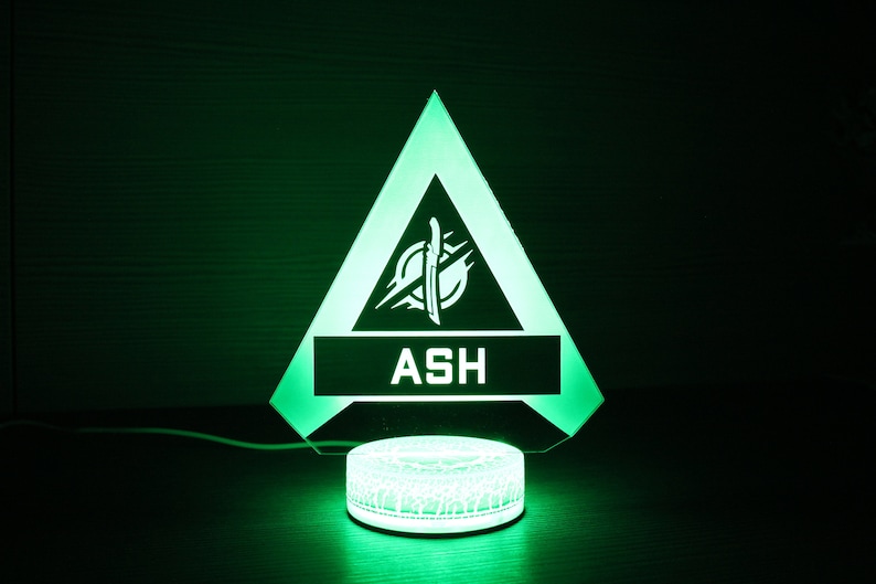 May include: A green triangle-shaped LED night light with a white logo and the word "ASH" in the center. The light is on a white circular base.