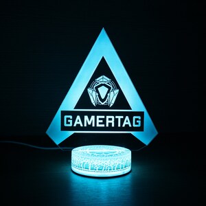 May include: A blue and white gamertag light with a triangle shape and a circular base. The light features a stylized logo and the word "GAMERTAG" in white.