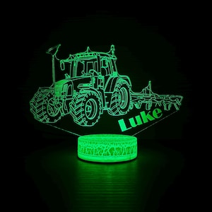 Puede incluir: Una luz nocturna de tractor verde brillante con el nombre "Luke" iluminado. El tractor es un contorno detallado, y la base tiene una textura agrietada. El fondo es negro.