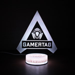 May include: A white acrylic lamp shaped like a triangle with a black logo that says "GAMERTAG" and a white circular base.