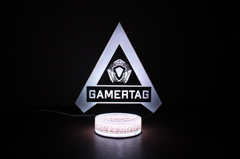 May include: A white acrylic lamp shaped like a triangle with a black logo that says "GAMERTAG" and a white circular base.