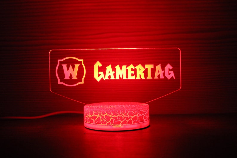 May include: A white and yellow acrylic sign with the text "W GAMERTAG" on a white base with a textured surface. The sign is illuminated with red light.
