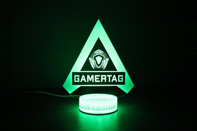 May include: A green illuminated triangle shaped lamp with a white gamertag logo and a white circular base with a geometric pattern.
