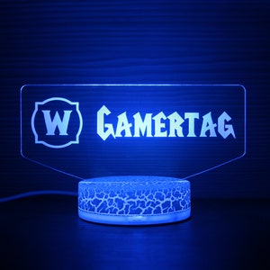 May include: A blue LED light with a clear acrylic panel displaying the text "W GAMERTAG". The light sits on a textured white base.