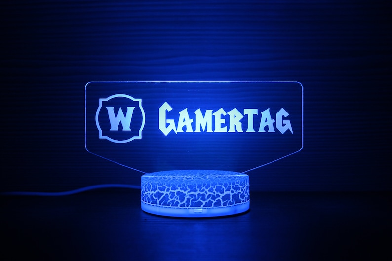 May include: A blue LED light with a clear acrylic panel displaying the text "W GAMERTAG". The light sits on a textured white base.