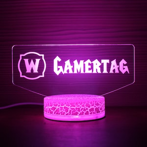 May include: A pink acrylic light-up sign with the text "W GAMERTAG" in a white font. The sign is on a round, white base with a textured surface.