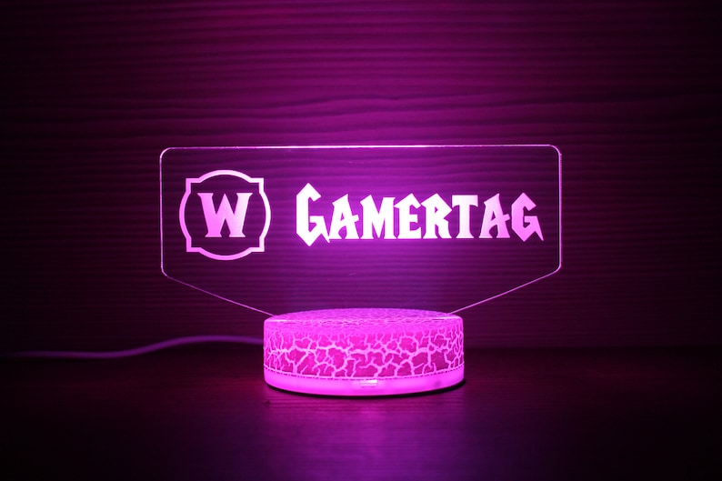May include: A pink acrylic light-up sign with the text "W GAMERTAG" in a white font. The sign is on a round, white base with a textured surface.