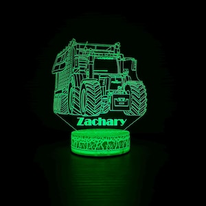 以下が含まれることがあります： 緑色のトラクター型のナイトライトで、「Zachary」という名前が緑色に光っています。 トラクターのデザインは詳細なアウトラインで、ベースにはテクスチャパターンがあります。 黒い背景に明るく光っています。