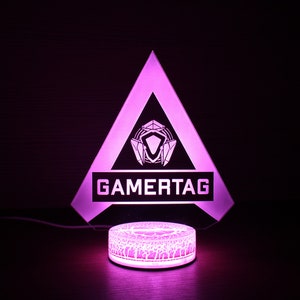 May include: A pink LED light with a triangular base and a white logo that says "GAMERTAG". The base has a geometric design.