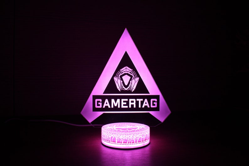 May include: A pink LED light with a triangular base and a white logo that says "GAMERTAG". The base has a geometric design.