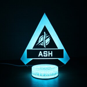 May include: A blue and white light-up lamp shaped like a triangle with the word "ASH" and a symbol inside. The lamp is on a circular base.