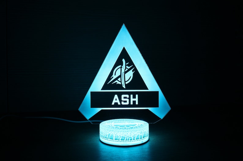 May include: A blue and white light-up lamp shaped like a triangle with the word "ASH" and a symbol inside. The lamp is on a circular base.