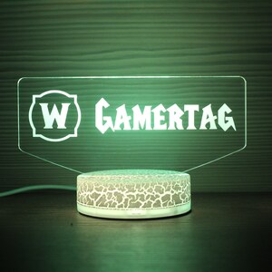 May include: A green LED light with a white base and a clear acrylic panel with the text "W GAMERTAG" in white.