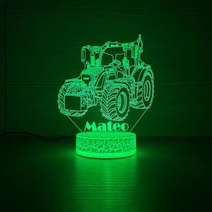 Puede incluir: Luz de noche LED verde con forma de tractor y el nombre "Mateo" grabado en la base. El tractor, un contorno detallado iluminado en verde, se asienta sobre una base circular texturizada. Diseñado como pieza decorativa.