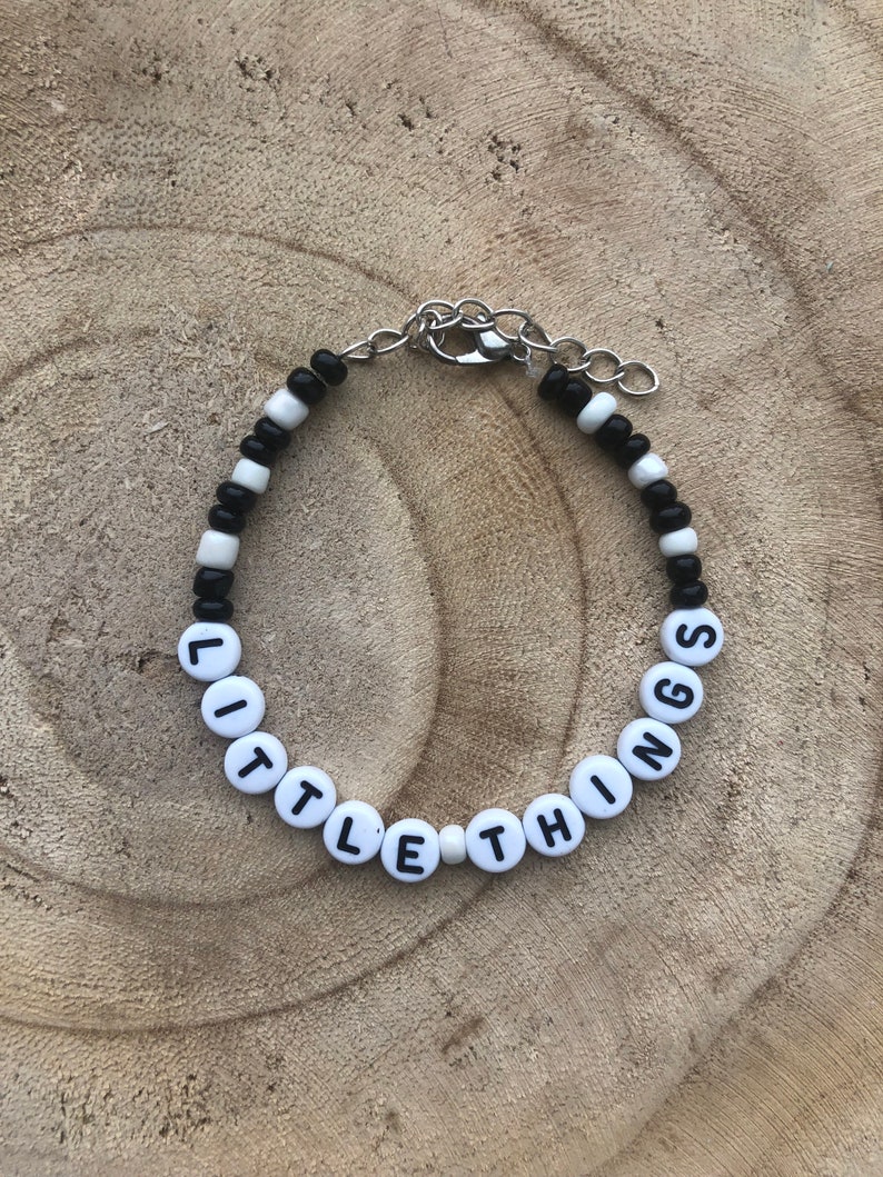 May include: A beaded bracelet with the words "LITTLE THINGS" spelled out in white letter beads. The bracelet also features black and white beads and a silver-colored clasp.