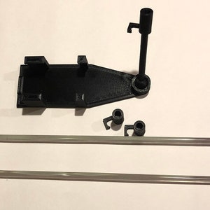 May include: A 3D printed black plastic stand with two clear plastic rods. The stand has a base with a circular hole and a vertical post with a hook at the top. The rods are about 12 inches long.