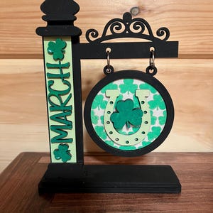 Puede incluir: Un letrero de madera negro con un trébol verde y un diseño de herradura. El letrero dice "Marzo" y es perfecto para el Día de San Patricio.