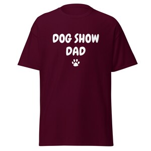 May include: Burgundy t-shirt with white text that reads "Dog Show Dad" and a white paw print.